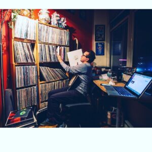 DJ near a large book case of vinyls.